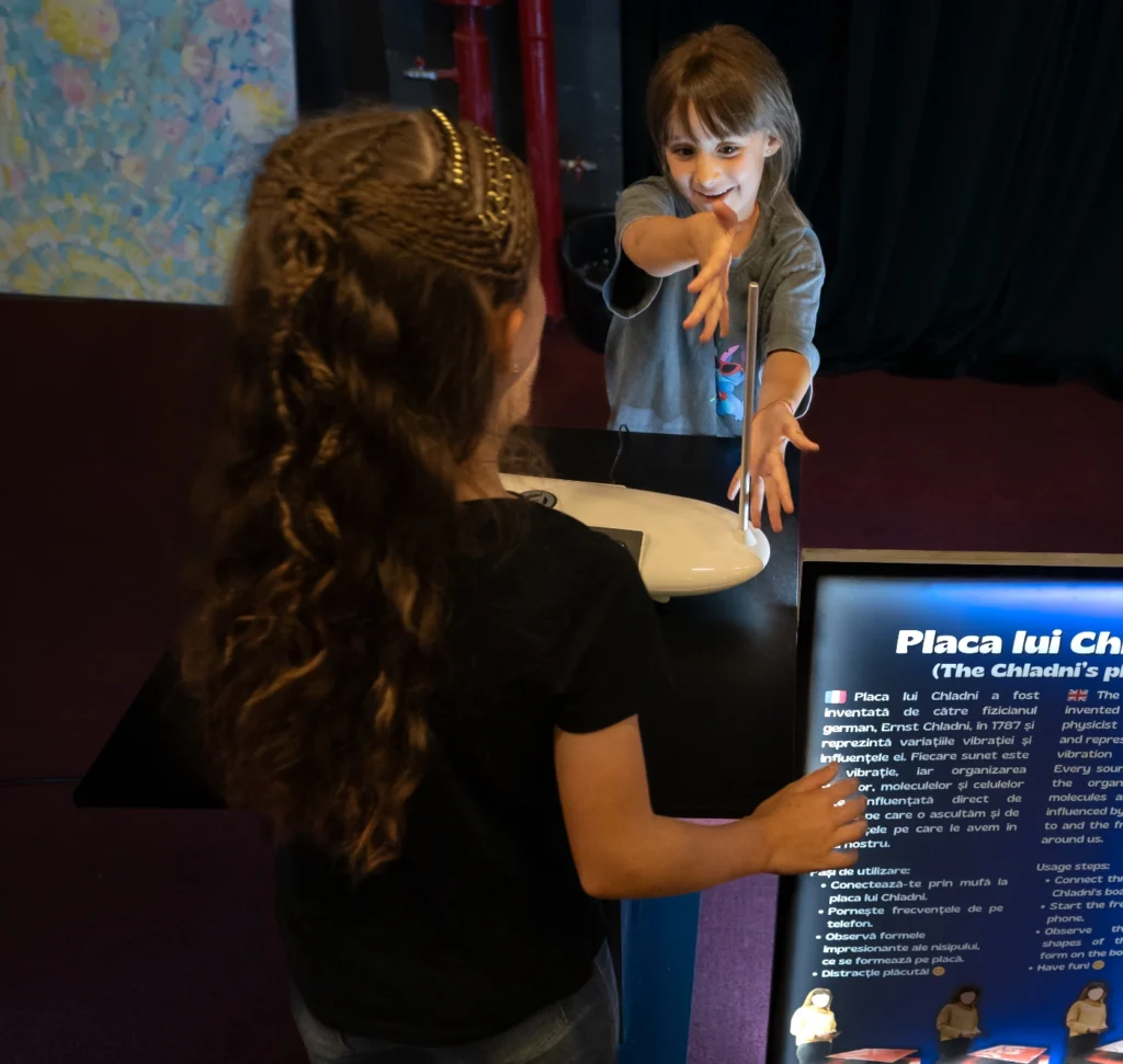 Copiii experimentează Tabla lui Chladni și află cum frecvențele „desenează” modele.
